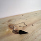 A zoomed out view of a black obsidian pendulum sitting on a pine board with a white backdrop.