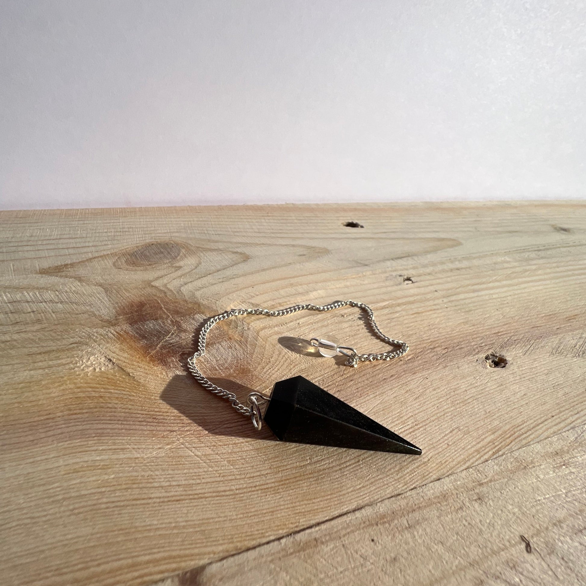 A black obsidian pendulum sitting on a piece of pine board.