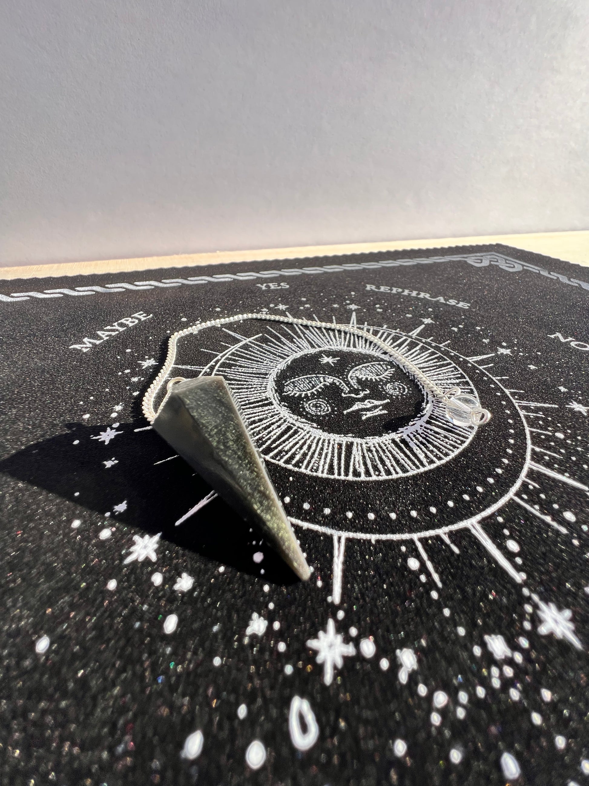 A black obsidian pendulum sitting on a celestial pendulum mat.