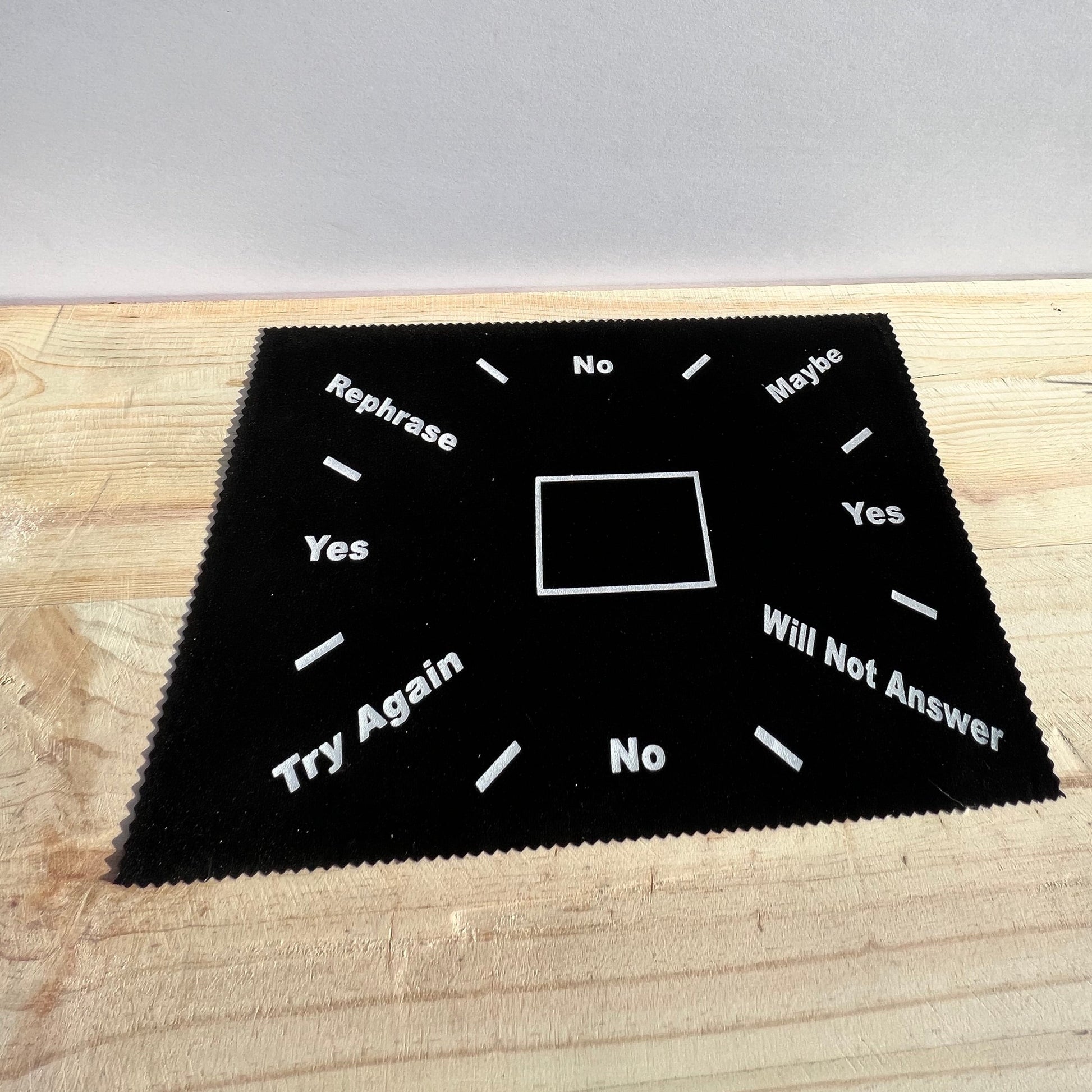 A basic pendulum mat featuring a center square, with "No" written at the top & bottom, "Yes" on the left and right, "rephrase", "maybe", "try again", and "will not answer" appear diagonally.