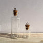 A large and small glass spell jar with eyelet hooks.